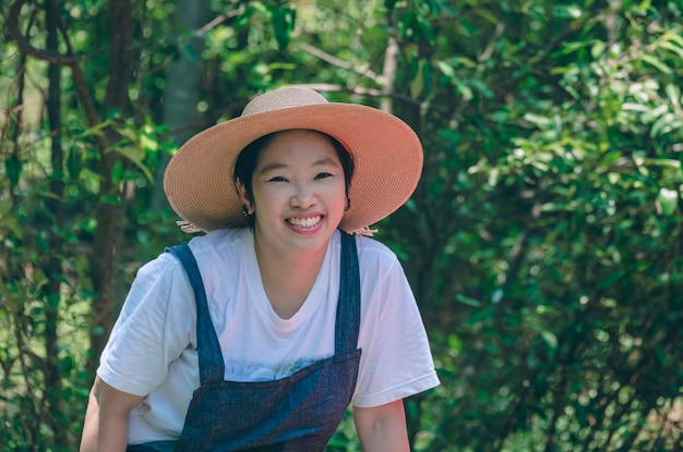 Turista asiática com chapéu sorrindo e olhando para a câmera enquanto ecoturismo no parque natural