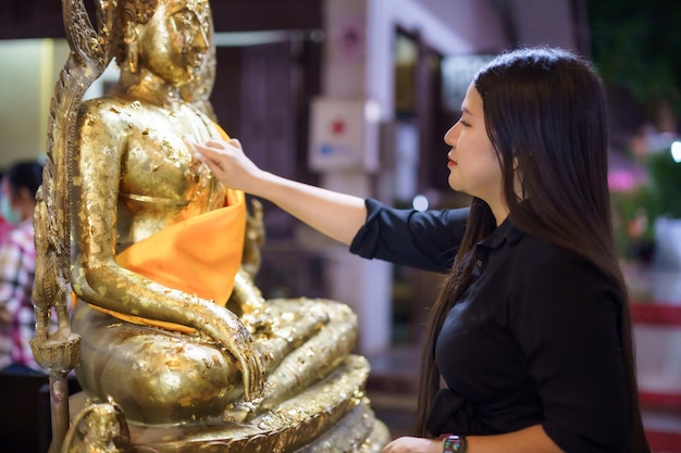 Turista asiática Dourando folha de ouro a Buda para adoração com fé à estátua de Buda no templo Tailândia crença no budismo