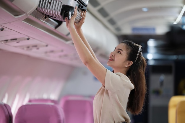 Foto una turista asiática empaca su maleta en un estante dentro del avión.