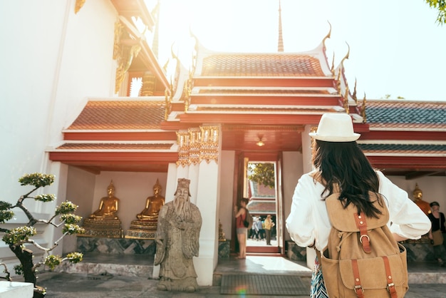 Turista asiática feminina caminhando para o antigo templo na tailândia. ela fica na frente do portão, em uma visão traseira.