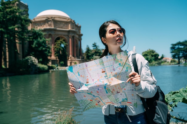 una turista asiática perdida sostiene un mapa en busca de direcciones mientras visita el palacio de bellas artes junto al estanque en un día soleado en San Francisco, California, EE.