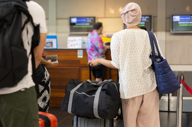 Turista asiática de pie con equipaje en el mostrador de facturación en la terminal del aeropuerto