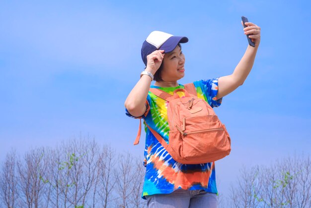 Turista asiática sonriendo alegremente y usando un teléfono inteligente tomando selfie en un parque natural