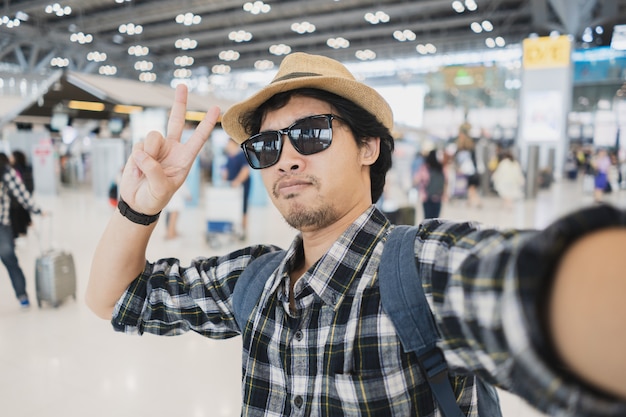 Turista asiático del hombre que toma un selfie con la cámara del teléfono elegante en aeropuerto.