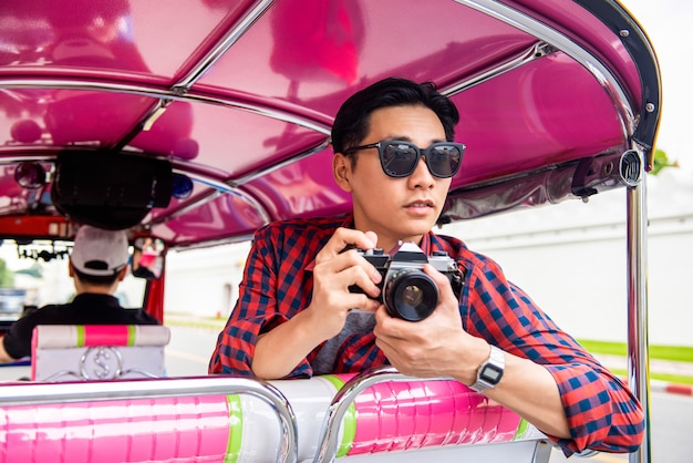 Turista asiático masculino guapo sosteniendo la cámara en tuk tuk taxi en Bangkok, Tailandia durante las vacaciones de verano viajando solo