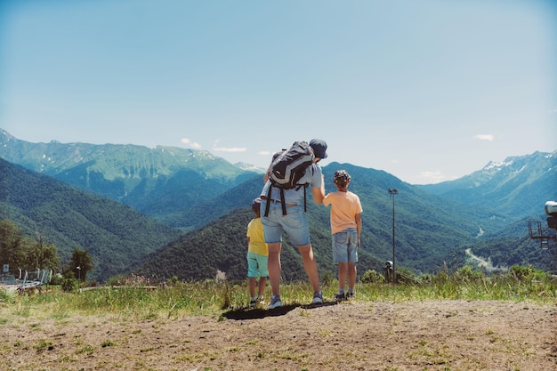 Foto turista barbudo milenar mostrando meninos em altas montanhas viajando em caminhadas com crianças