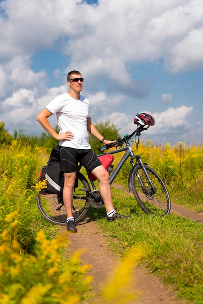 Un turista con una bicicleta se encuentra en el fondo de la hierba verde en verano