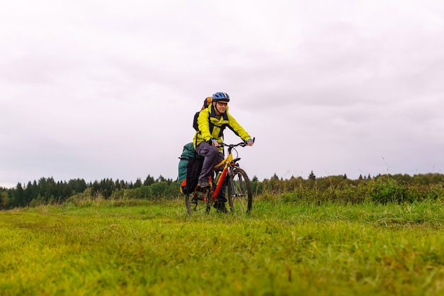 Foto turista en bicicleta masculino en un camino de tierra a través de un campo en un nublado día de otoño