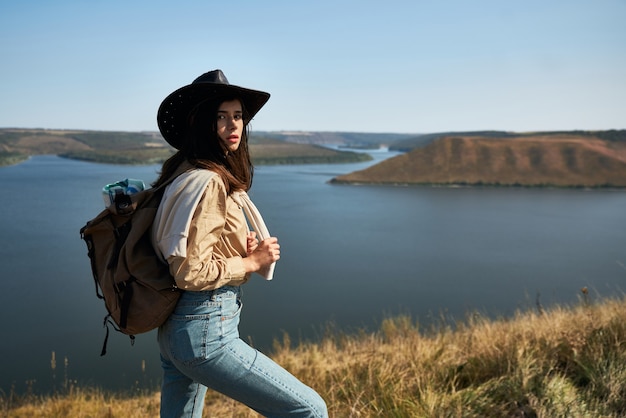 Turista bonita com chapéu de cowboy caminhando com mochila ao ar livre