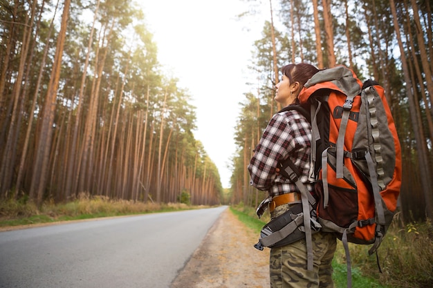 Turista cansada caminando por la carretera con mochila grande. Turismo nacional, viajes independientes solos, autostop, senderismo, transporte, esperando un paseo en una carretera vacía