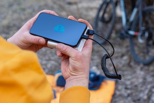 un turista carga un teléfono inteligente con un banco de energía en el fondo de una bicicleta en la naturaleza.