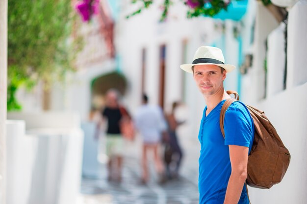 Turista caucásico caminando por las estrechas calles de Mykonos. Joven urbano de vacaciones explorando la calle de adoquines de la ciudad europea