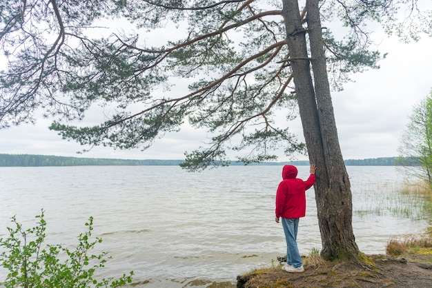 Un turista con una chaqueta cortavientos roja se encuentra en la orilla del lago