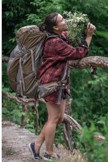 Turista chica atractiva con una mochila grande para viajar y con un ramo de flores silvestres.