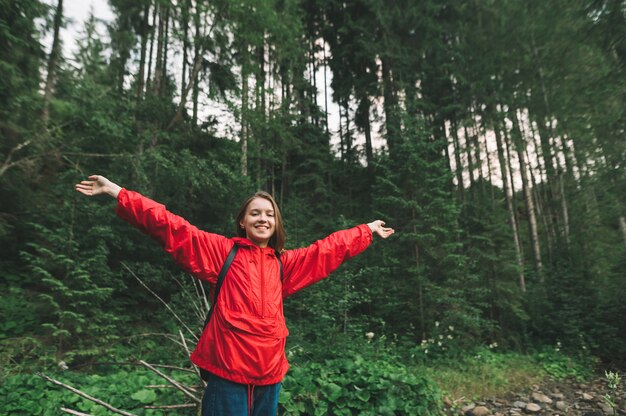 Turista chica en impermeable rojo se encuentra en registro en el bosque cerca del arroyo de montaña