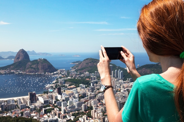 Turista chica toma una fotografía del paisaje de Río y Pao de Asucar con smartphone, Brasil