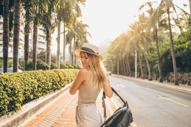 Turista chinês andando nas ruas da cidade no turismo de férias na Ásia. Mulher bonita caucasiana no chapéu com mochila viajar conceito de estilo de vida. Rua andando, palmeiras verdes e rodovia em Sanya, Hainan.