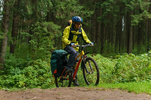 Foto turista ciclista masculino equipado cruza un barranco en un bosque de abetos con aceleración