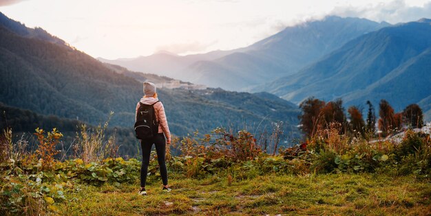 Turista com mochila aprecia o pôr do sol no topo da montanha