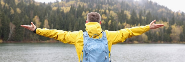 Turista com mochila e mãos abertas em pé perto do lago no dia chuvoso de outono felicidade liberdade