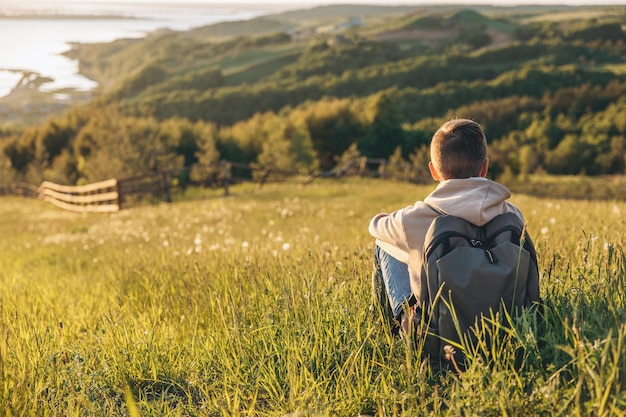 Turista com mochila sentado no topo da colina no campo de grama e apreciando a bela paisagem vista traseira do alpinista adolescente descansando na natureza Estilo de vida ativo Conceito de viagens locais