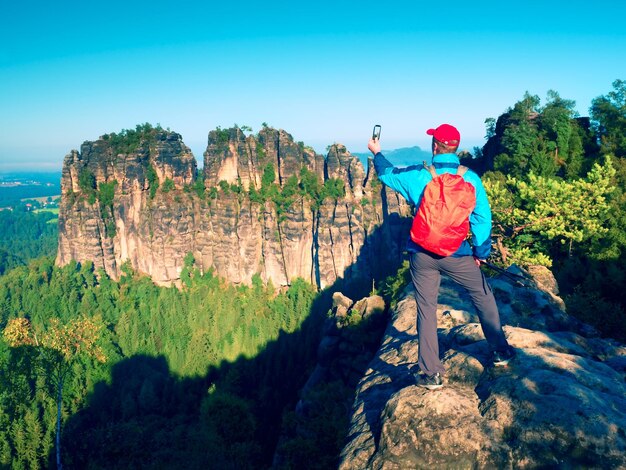 Foto turista com mochila vermelha tira fotos com telefone inteligente de rochas e vale