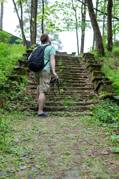 Turista com uma câmera nas mãos e uma mochila da cidade fica na frente dos antigos degraus de pedra