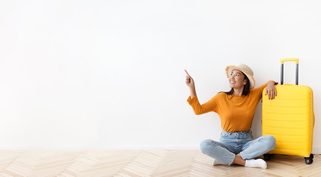 Turista coreana positiva com mala apontando para o espaço de cópia