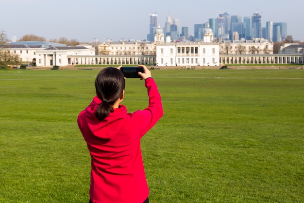 Turista da mulher que toma imagens do edifício no parque com telefone celular.