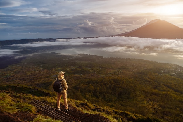 Turista de homem olha para o nascer do sol no vulcão Batur, na ilha de Blai, na Indonésia. Homem alpinista com mochila viajar no topo do vulcão, conceito de viagens