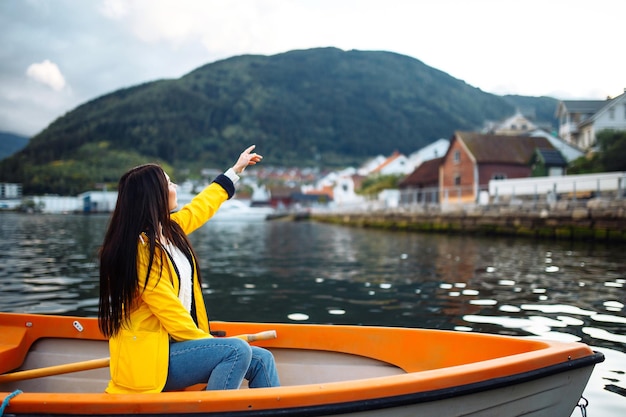 Turista de jaqueta amarela está sentada e posando em um barco contra o pano de fundo das montanhas