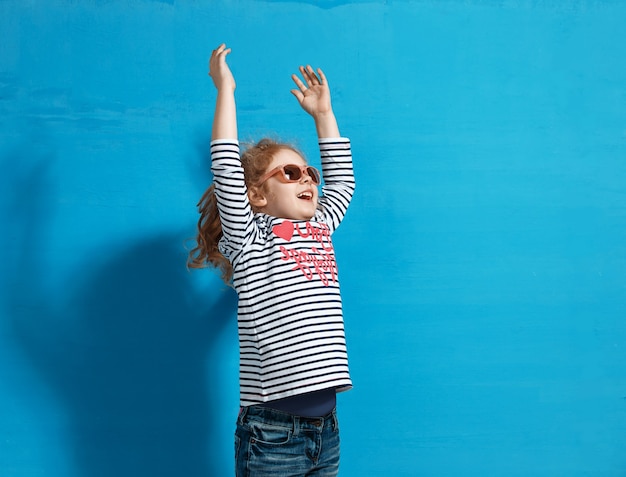 Turista de menina criança feliz em óculos de sol rosa na parede azul. Conceito de viagens e aventura.