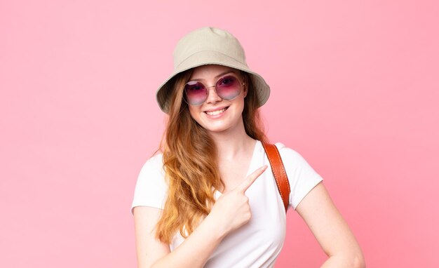 Turista de mulher bonita ruiva sorrindo alegremente, sentindo-se feliz e apontando para o lado