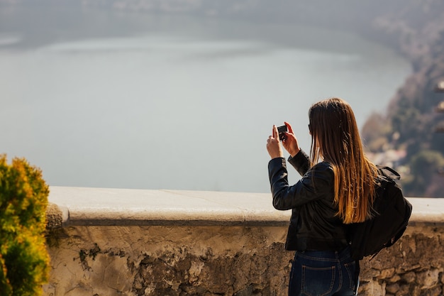 Turista de mulher com cabelo comprido, tirando foto com smartphone no topo de uma montanha de viajar na Itália.