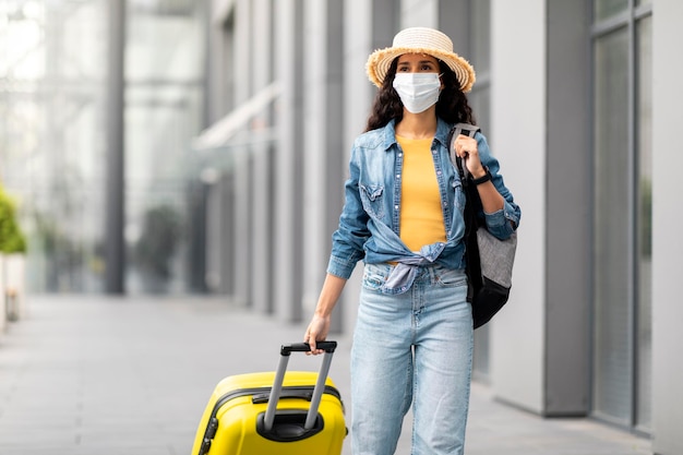 Turista de mulher com máscara facial com mala andando pelo aeroporto