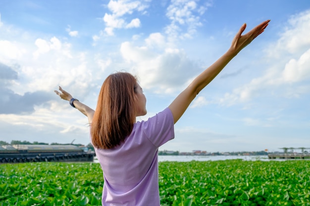 Turista de mulher feliz em pé e levante as mãos na planta verde com céu azul