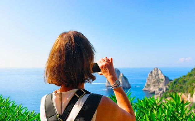 Turista de mulher na Marina Piccola na ilha de Capri, Itália, em Nápoles. Paisagem com pessoa no mar Mediterrâneo na costa italiana. Anacapri, Europa. Vista em Faraglioni. Cenário de Amalfi e montanha Solaro