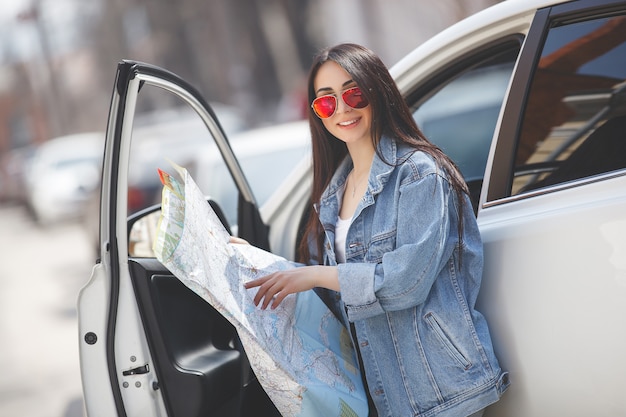 Turista de mulher segurando um mapa da cidade. Viajante de carro navegando no país desconhecido. Menina dirigindo um carro.