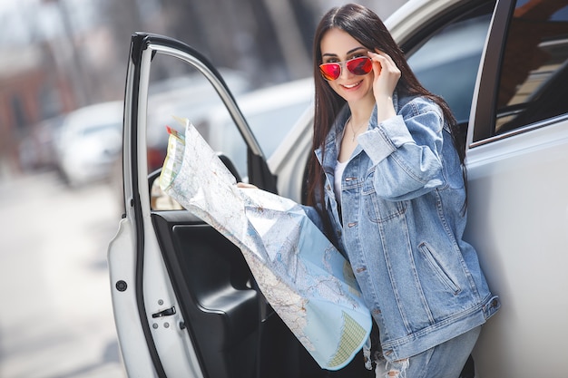 Turista de mulher segurando um mapa da cidade. Viajante de carro navegando no país desconhecido. Menina dirigindo um carro.