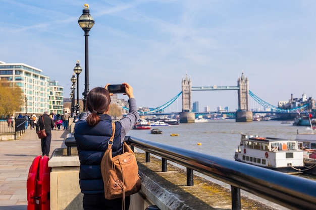 Turista de mulher tirando foto na Tower Bridge com a câmera do telefone móvel.