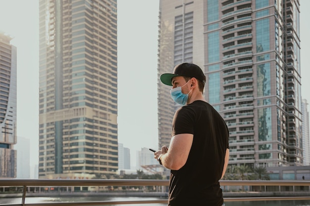 Foto turista de pessoa com máscara médica segurando e usando telefone digitando mensagens enquanto está ao ar livre