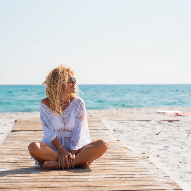 Turista de pessoas do sexo feminino feliz witting em um píer de madeira na praia na areia aproveitando as férias de verão e incrível destino tropical Água azul do oceano no fundo Uma mulher senta e sorri