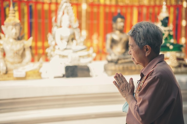 Turista de viajante sênior asiática idosa rezando no templo budista.