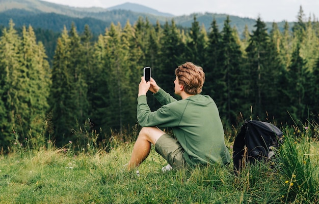 Turista descansando em uma caminhada sentado em um prado e usando a Internet em um smartphone