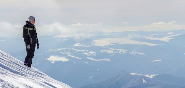 turista em pé no topo de uma montanha de neve, apreciando a vista e a realização em um dia ensolarado de inverno.