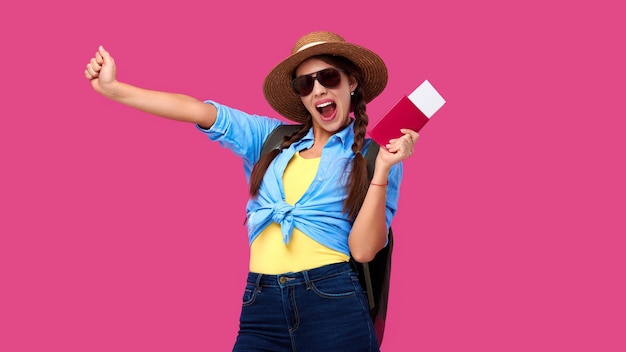 Turista emocionada con pasaporte y boletos de viaje sobre fondo aislado rosa Estudiante en ropa casual de verano Mujer caucásica sonriente con gafas de sol