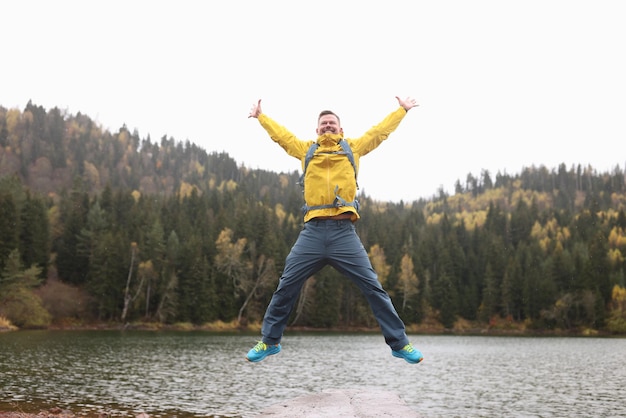 Un turista emocionado salta a la orilla de un gran lago en el bosque salvaje el día de otoño, el hombre positivo explora