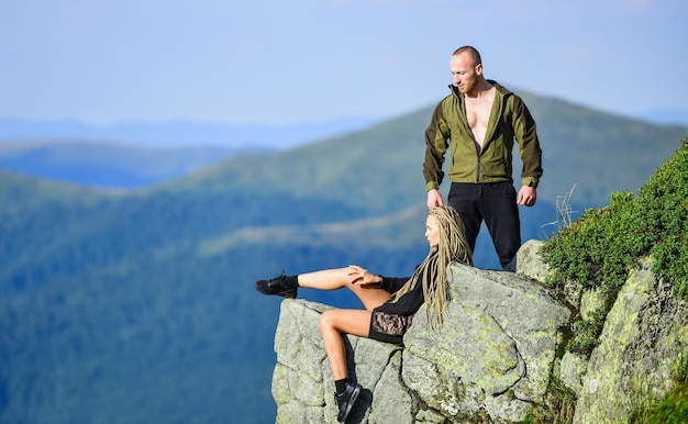 Turista excursionista niña y hombre relajante Beneficios de senderismo Fin de semana de senderismo En el borde del mundo Mujer sentada al borde del acantilado Fondo de paisaje de montañas altas Pareja de excursionistas disfruta de la vista Senderismo momento de paz