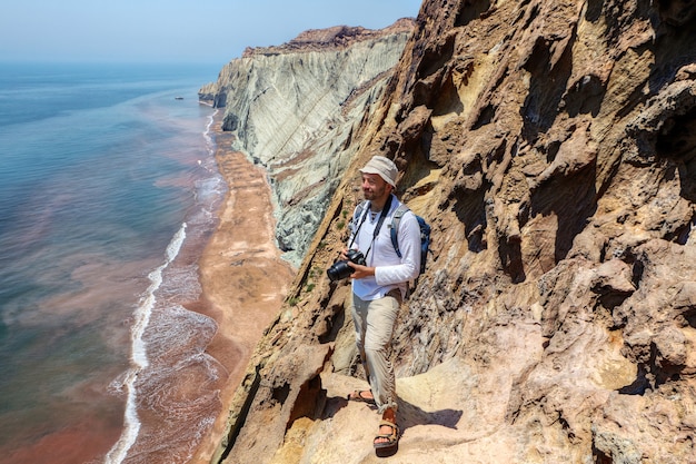 Turista feliz con cámara se encuentra en el borde del acantilado, la isla de Hormuz, Hormozgan, Irán.