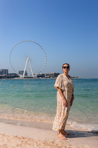 Turista feliz camina descalza en una playa de arena en el área de JBR de Dubai y admira la vista panorámica de la rueda de la fortuna de Ain